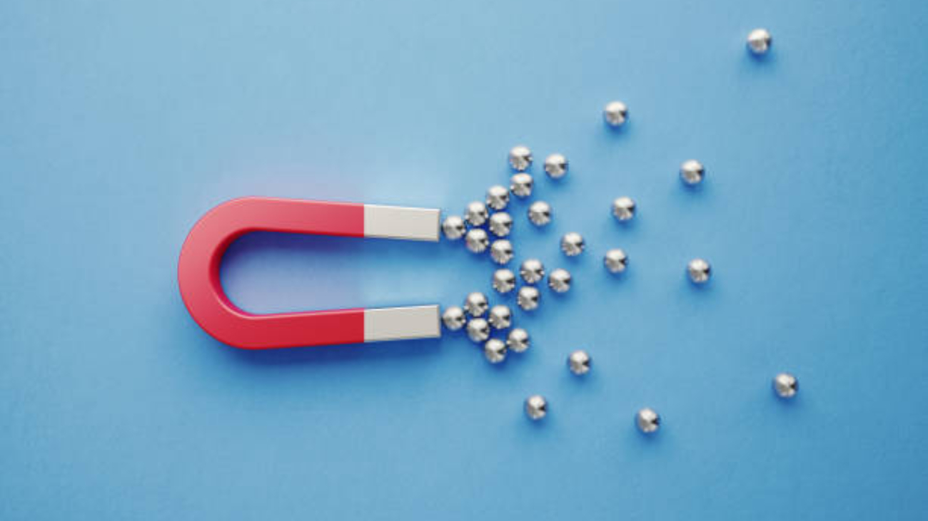 Silver spheres gravitated towards a red magnet on blue background. Horizontal composition with copy space. Digital marketing concept.